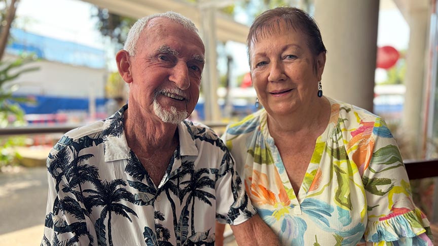 A woman and a man sitting beside each other holding hands smiling at the camera