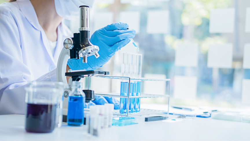 Researcher wearing gloves sitting behind a microscope and specimen beakers