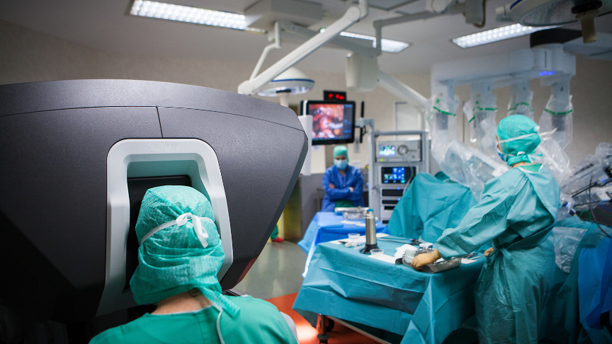 Three clinicians in scrubs standing in a surgical theatre, one looking into a large piece of equipment