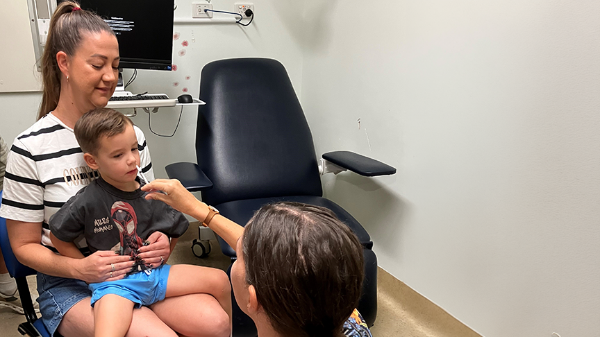 Young boy sitting on mother's lap with nurse holding nasal spray to child's nose