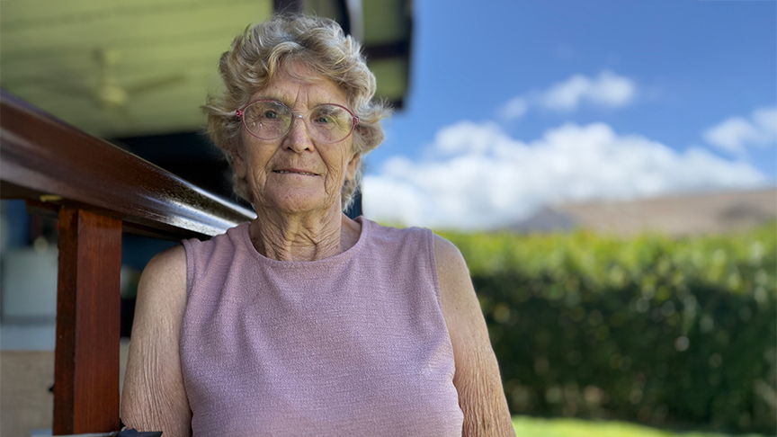 Older woman standing in her backyard looking at camera smiling