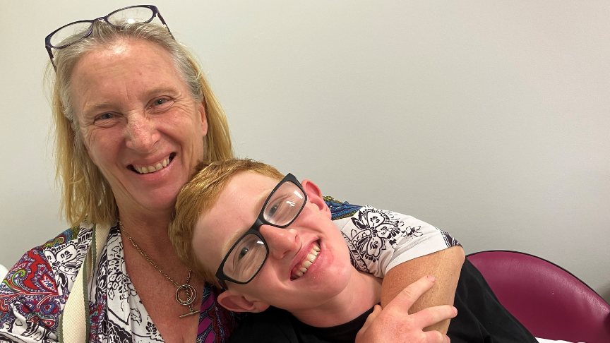 Smiling teenage boy leaning into his mother who has her arm around him
