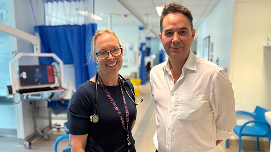 One male and one female clinician standing in the hallway of a ward smiling at the camera
