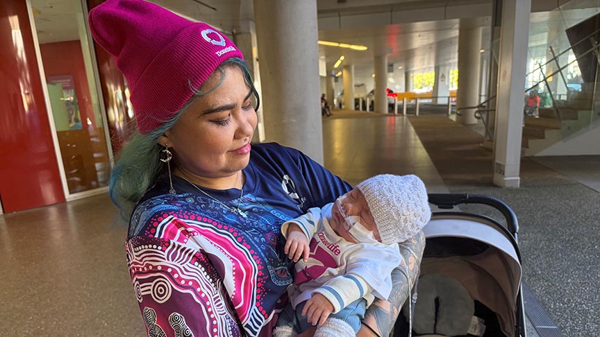 Mother looking down at newborn baby in her arms, mother wearing a pink Donate Life beanie and baby wearing Donate Life onesie