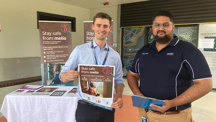 Two men standing in front of a table and pull-up banners advertising Melioidosis