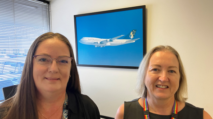 Close up of two smiling women with an image of an old Ansett plane on the wall between them